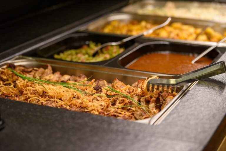 Im Hotel Bodenmais erwartet Sie ein reichhaltiges Buffet mit Tabletts voller gekochtem Fleisch, Gemüse und Soßen. Servierzangen liegen elegant auf einem Tablett und laden die Gäste zu einem kulinarischen Erlebnis der besonderen Art ein.