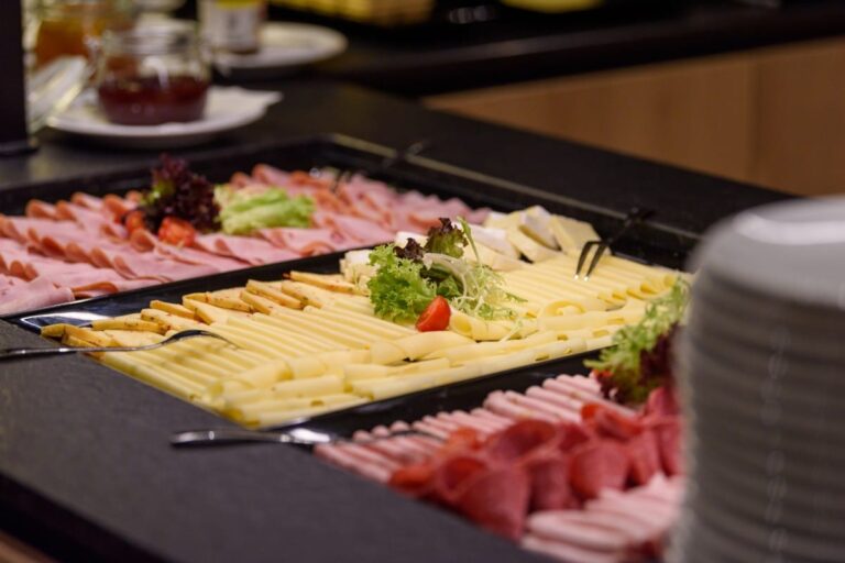 Verwöhnen Sie sich im Hotel Bodenmais mit einem Buffet mit verschiedenen Aufschnitt- und Käsescheiben, kunstvoll auf einer Platte angerichtet und mit frischem Salat und Tomaten garniert.