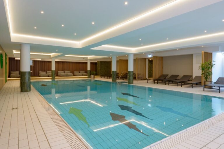 Erleben Sie den großzügigen Innenpool des Hotels Bodenmais mit seinen dekorativen Bodenfliesen und luxuriösen Liegestühlen rund um die Terrasse, die zum Entspannen und Erholen einladen.