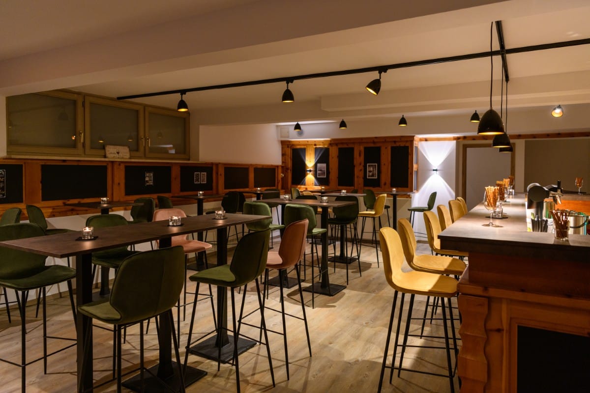 Im Hotel Bodenmais befindet sich eine moderne Bar mit hohen Tischen, farbenfrohen Stühlen und gedämpftem Licht, die eine gemütliche Atmosphäre schafft.